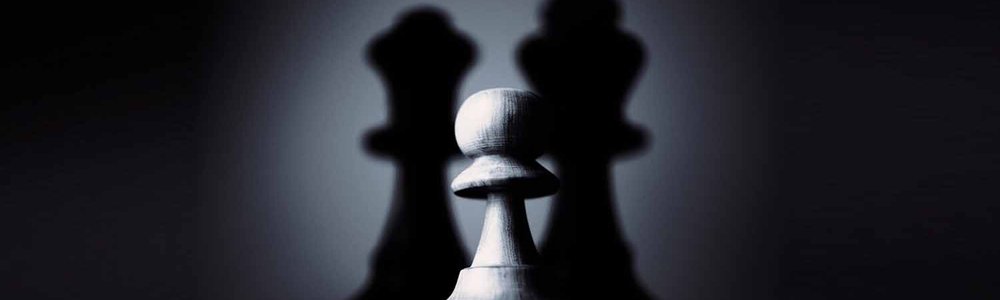 Photo of a pawn in the shadows of the king and queen pieces