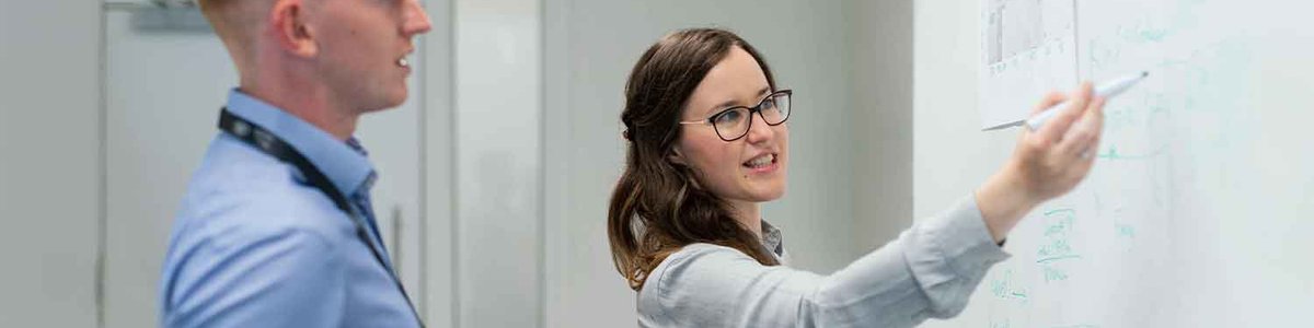 A photo of two colleagues conversing about work on a white board