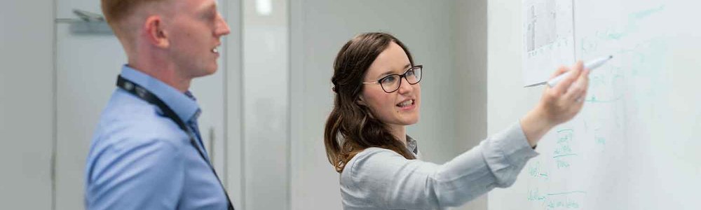 Une photo de deux collègues discutant de leur travail sur un tableau blanc.
