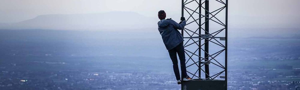 Personne grimpant sur une tour cellulaire avec la ville en arrière-plan||||