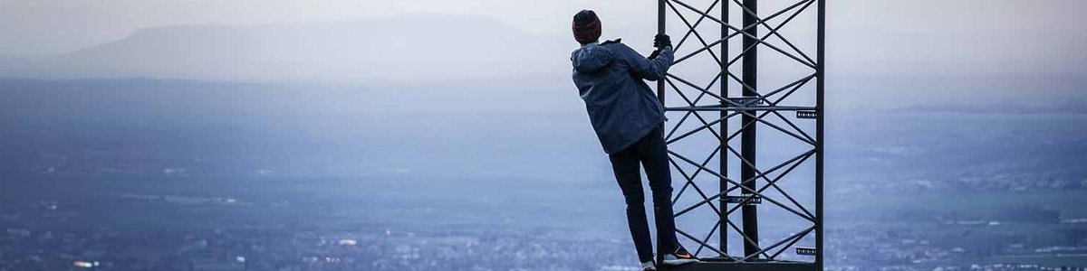 Personne grimpant sur une tour cellulaire avec la ville en arrière-plan||||