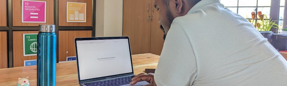 Man (Sadam Hanjabam) sitting at a laptop which shows a no Internet connection warning on the screen|