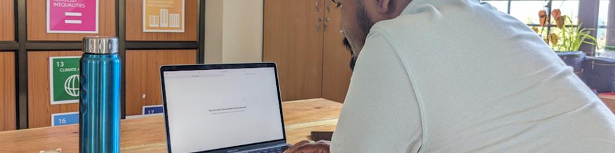 Man (Sadam Hanjabam) sitting at a laptop which shows a no Internet connection warning on the screen|