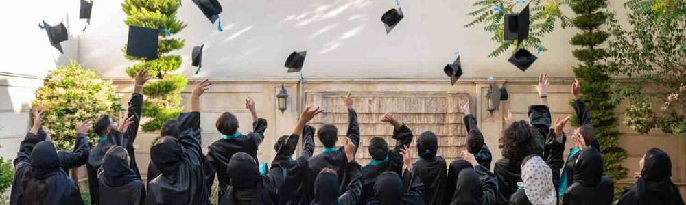 Photo of students in gowns throwing their mortar board hats into the air