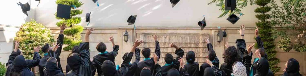 Photo of students in gowns throwing their mortar board hats into the air