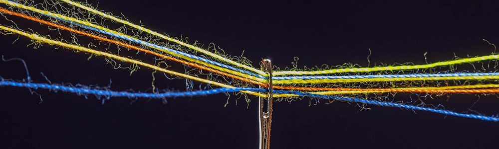 Photo of a needle with multiple threads through its eye.||