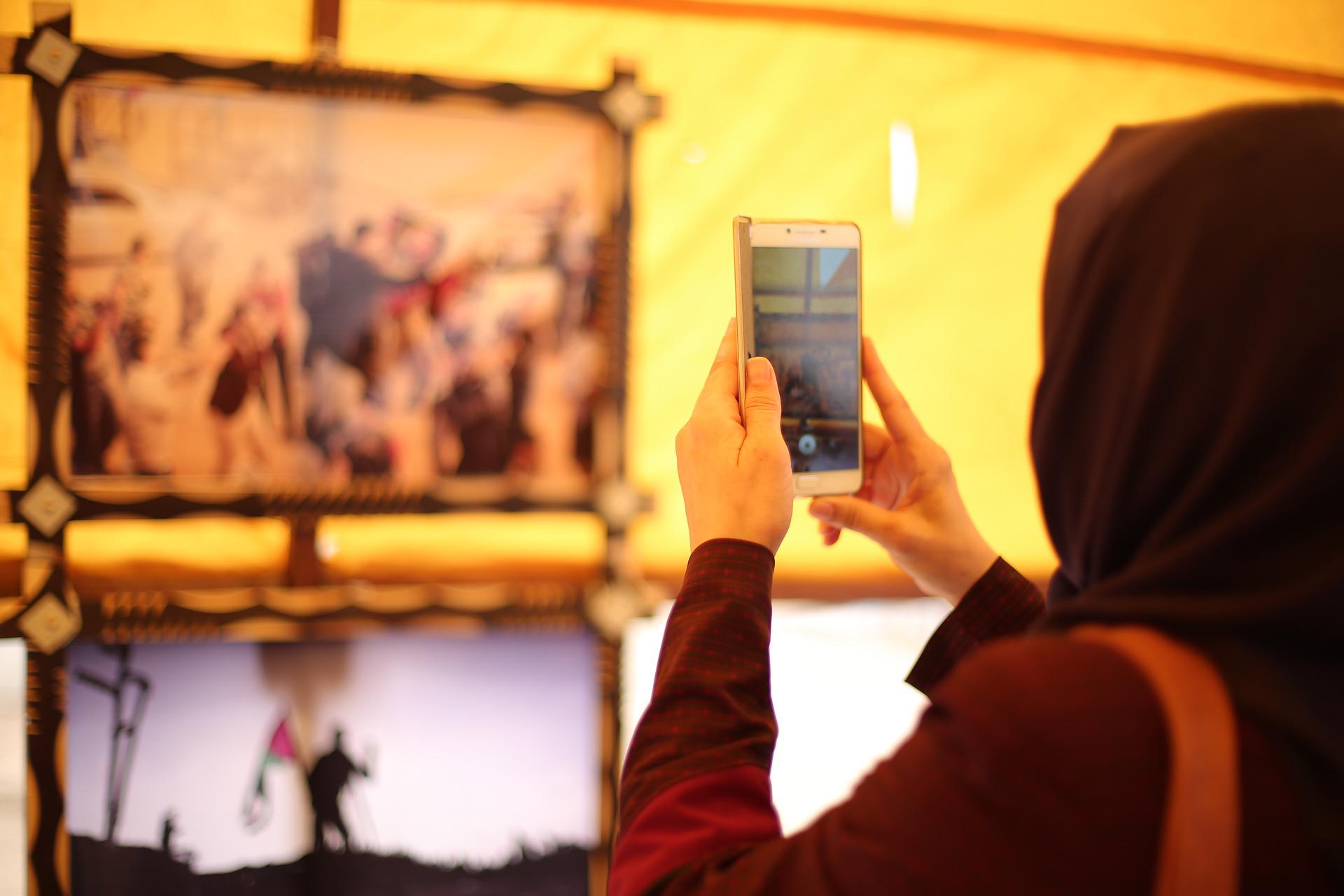 Une femme portant un hijab prend une photo avec un téléphone portable.