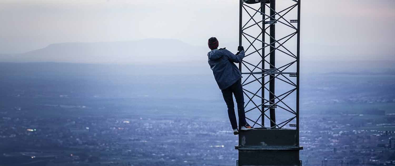 Person climbing a cell tower with city in the background