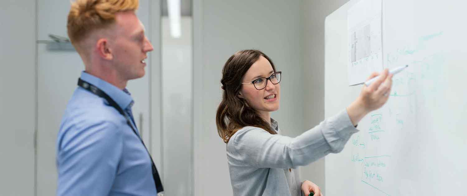 A photo of two colleagues conversing about work on a white board