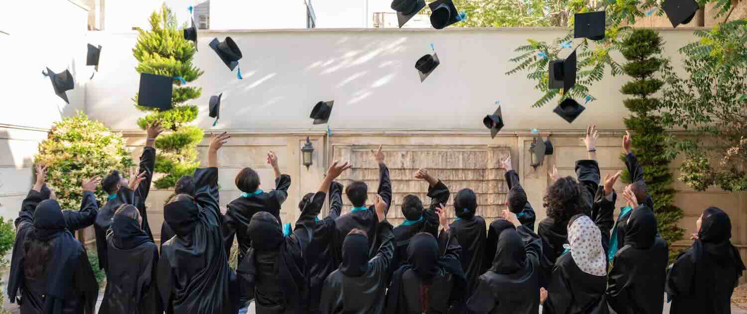 Photo of students in gowns throwing their mortar board hats into the air